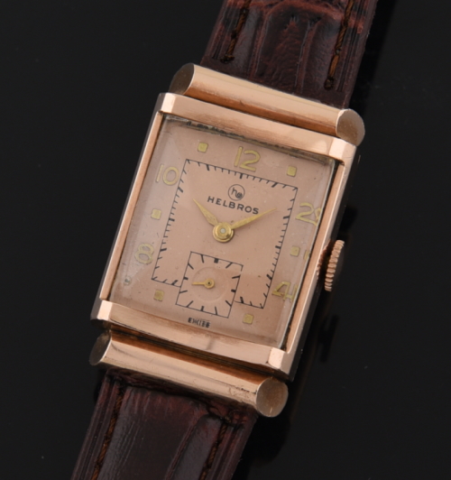 1950s Helbros 14k rose gold small watch with original salmon-toned dial, rose markers, hands, bar lugs, and manual winding Swiss movement.